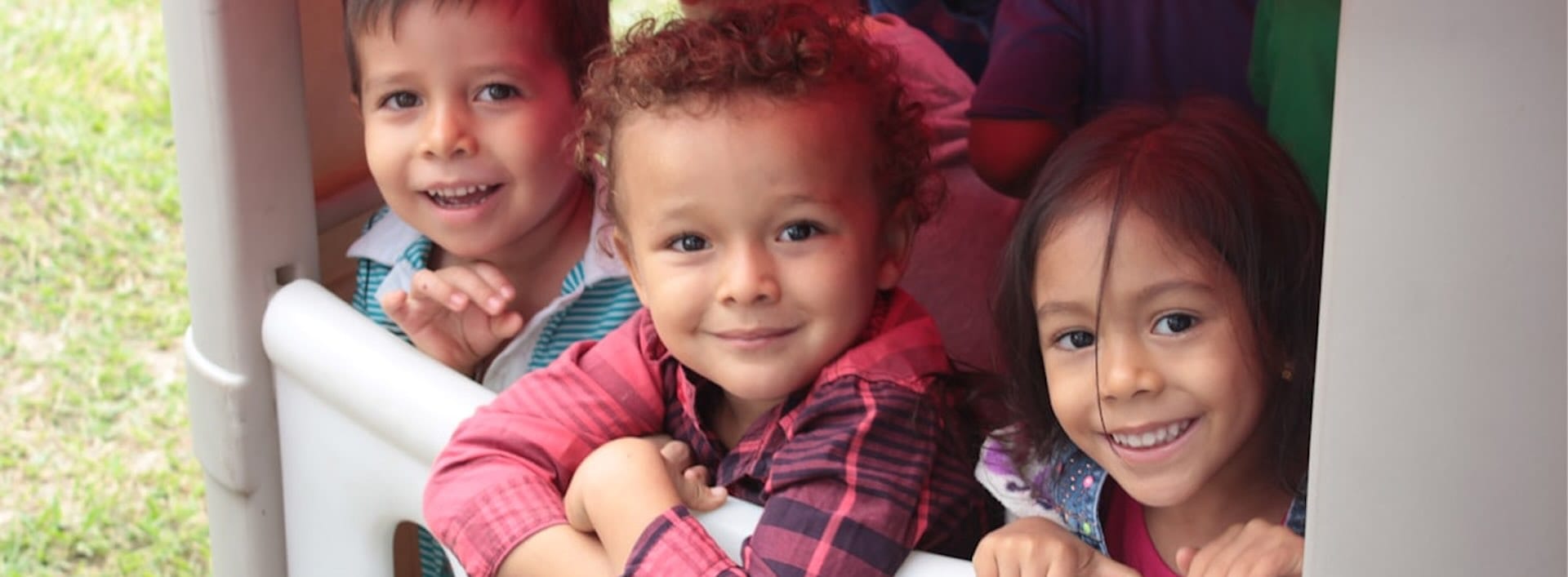 Three smiling children leaning out bus window