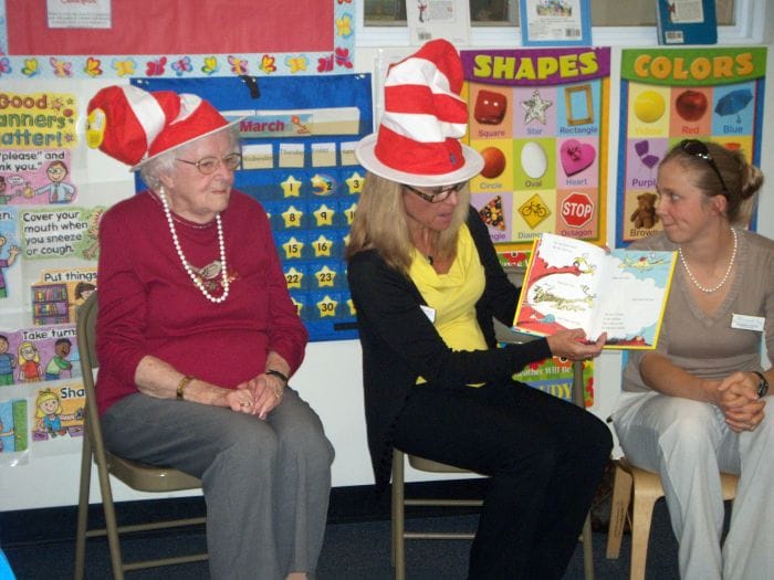 Adults wearing Dr. Seuss hats read to children.