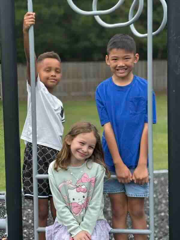Three children smiling on playground monkey bars