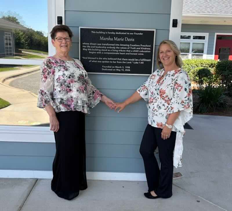 Two women standing beside dedication plaque outdoors